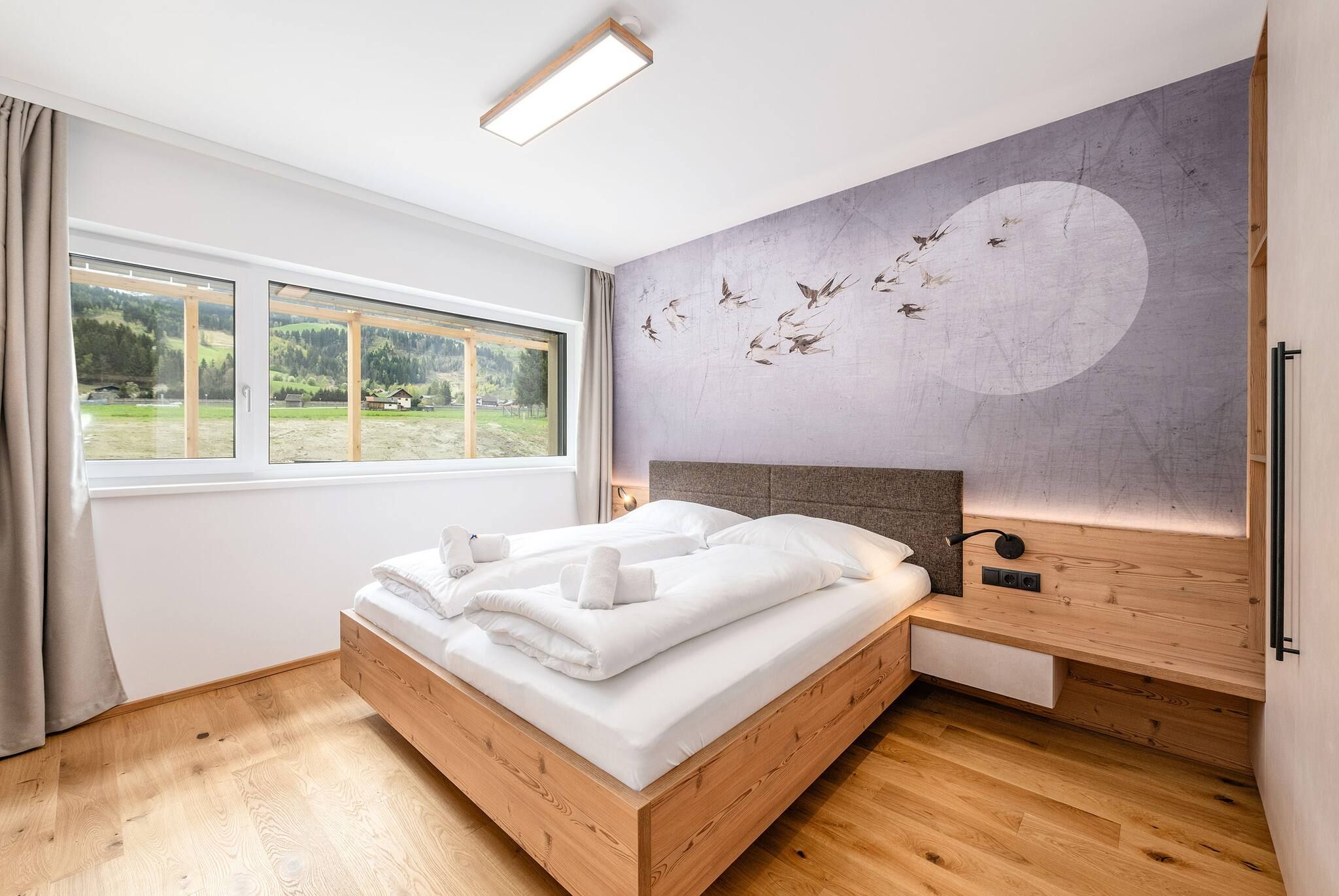 Ein Schlafzimmer mit Bett, Fenster, Wandgemälde und Nachttisch.
