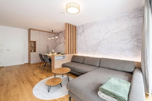 Ein modernes Wohnzimmer mit einer Eckcouch, einem Essbereich mit Tisch und Stühlen sowie einer Küche im Hintergrund.
