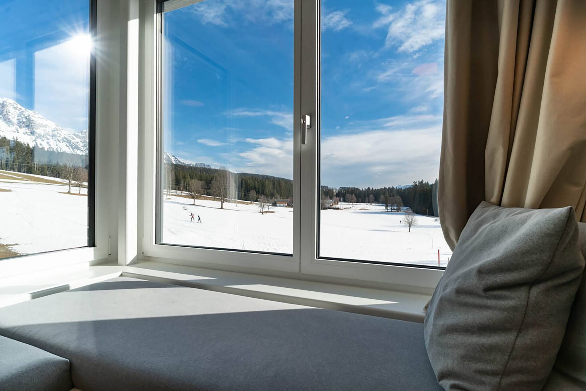 A window with a view of a snowy landscape, a sofa with a cushion, and a curtain.