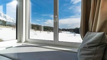 A window with a view of a snowy landscape, a sofa with a cushion, and a curtain.