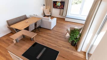 A modern living room with a wooden dining table, white sofas, and a flat-screen TV mounted on the wall.