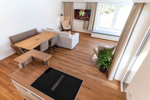 A modern living room with a wooden dining table, white sofas, and a flat-screen TV mounted on the wall. - Waldrand Apartments - Amsel 5 (Ramsau)