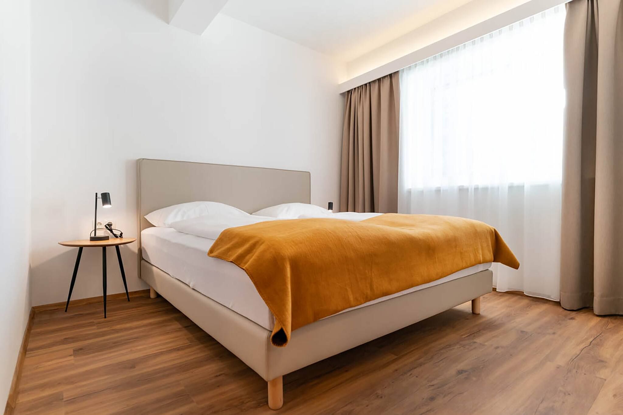 Une chambre moderne avec un lit, une table de chevet, une lampe et une fenêtre avec des rideaux.