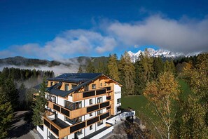 Ein mehrstöckiges Hotel mit modernem Design, das Balkone und große Fenster bietet, vor einer Kulisse aus Bergen und bewaldetem Gelände.