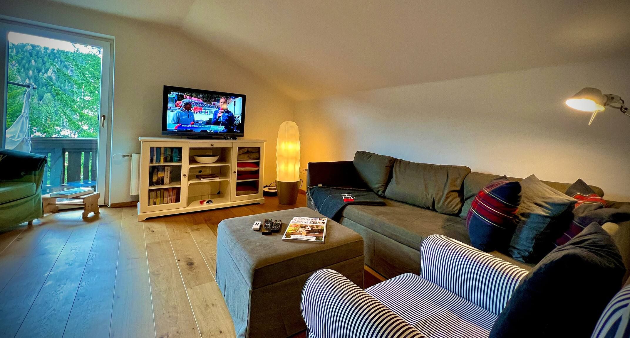 A living room with a television, sofa, ottoman, and a bookshelf.