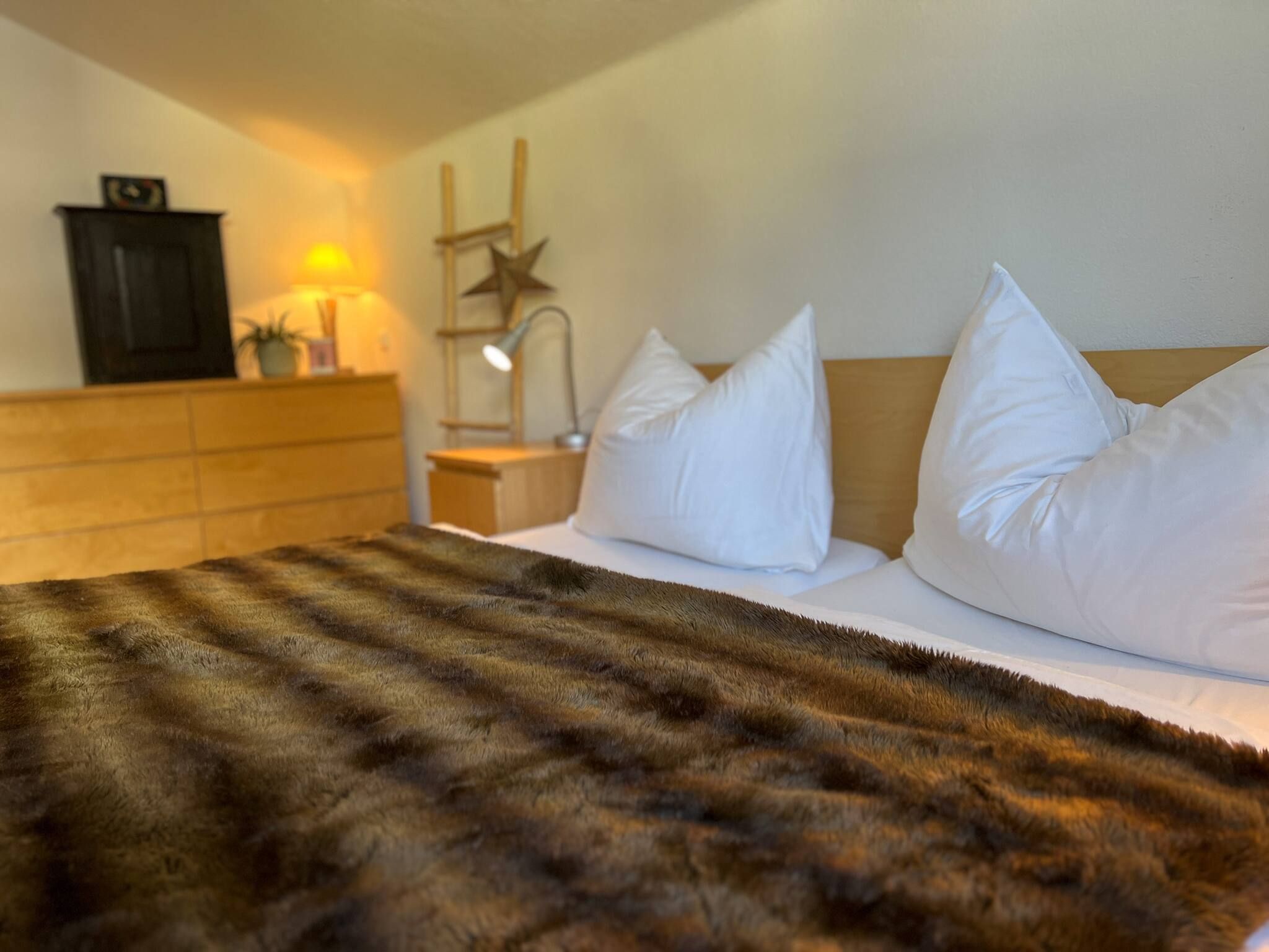 A hotel room with a bed, white pillows, a wooden headboard, a nightstand with a lamp, and a star decoration.
