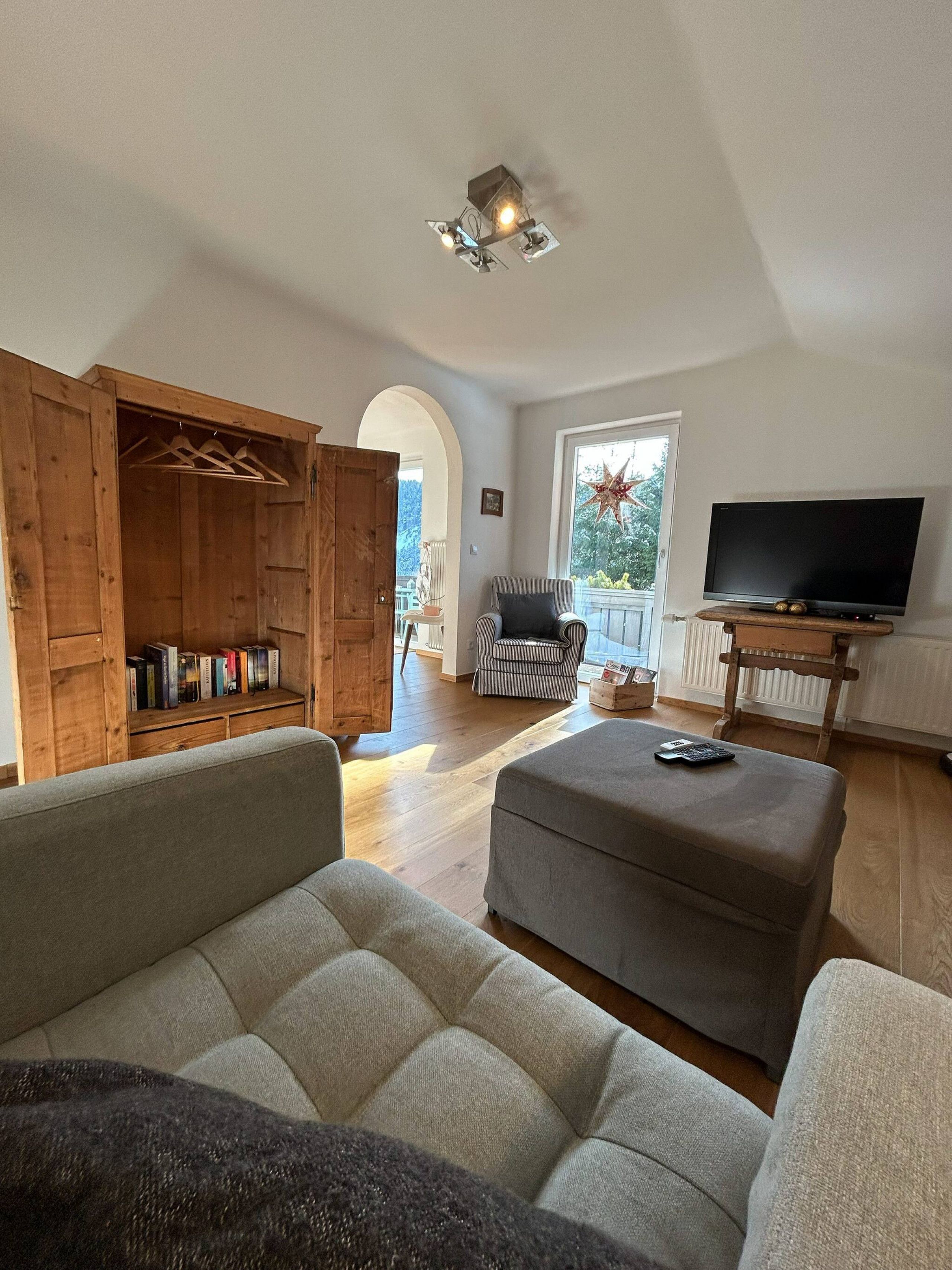 Ein Wohnzimmer mit einer Couch, Hocker, einem Holzschrank, einem Fernseher und einer Stern-Dekoration an der Wand.