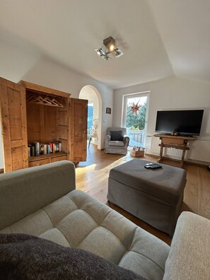 Una sala de estar con sofá, reposapiés, armario de madera, televisión y una decoración con forma de estrella en la pared.