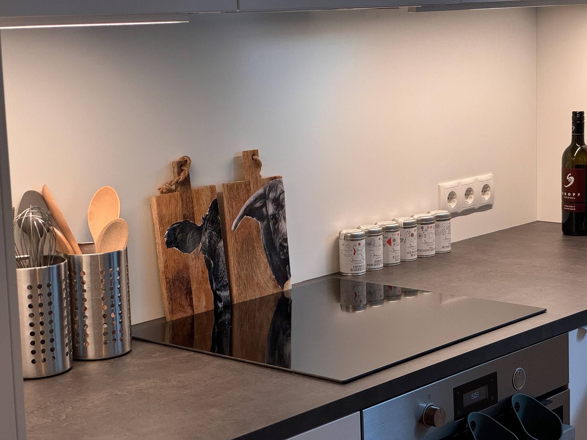 A kitchen with a black countertop, wooden cutting boards, a spice rack, and a bottle of wine.