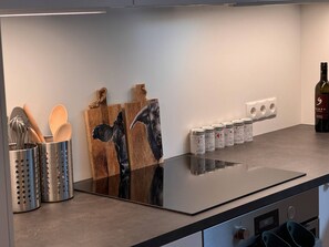 Eine Küche mit einer schwarzen Arbeitsplatte, Holzschneidebrettern, einem Gewürzregal und einer Weinflasche.