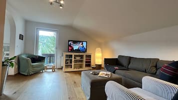 En stue med fjernsyn, sofa, lænestol og et lille bord med fjernbetjeninger.
