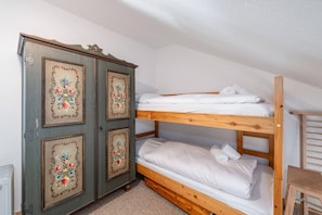 A bunk bed with white bedding, a wooden wardrobe with floral designs, and a small wooden chair. - Alpenblick Bad Mitterndorf 30 (Bad Mitterndorf)