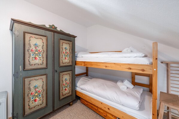 A bunk bed with white bedding, a wooden wardrobe with floral designs, and a small wooden chair. - Alpenblick Bad Mitterndorf 30 (Bad Mitterndorf)