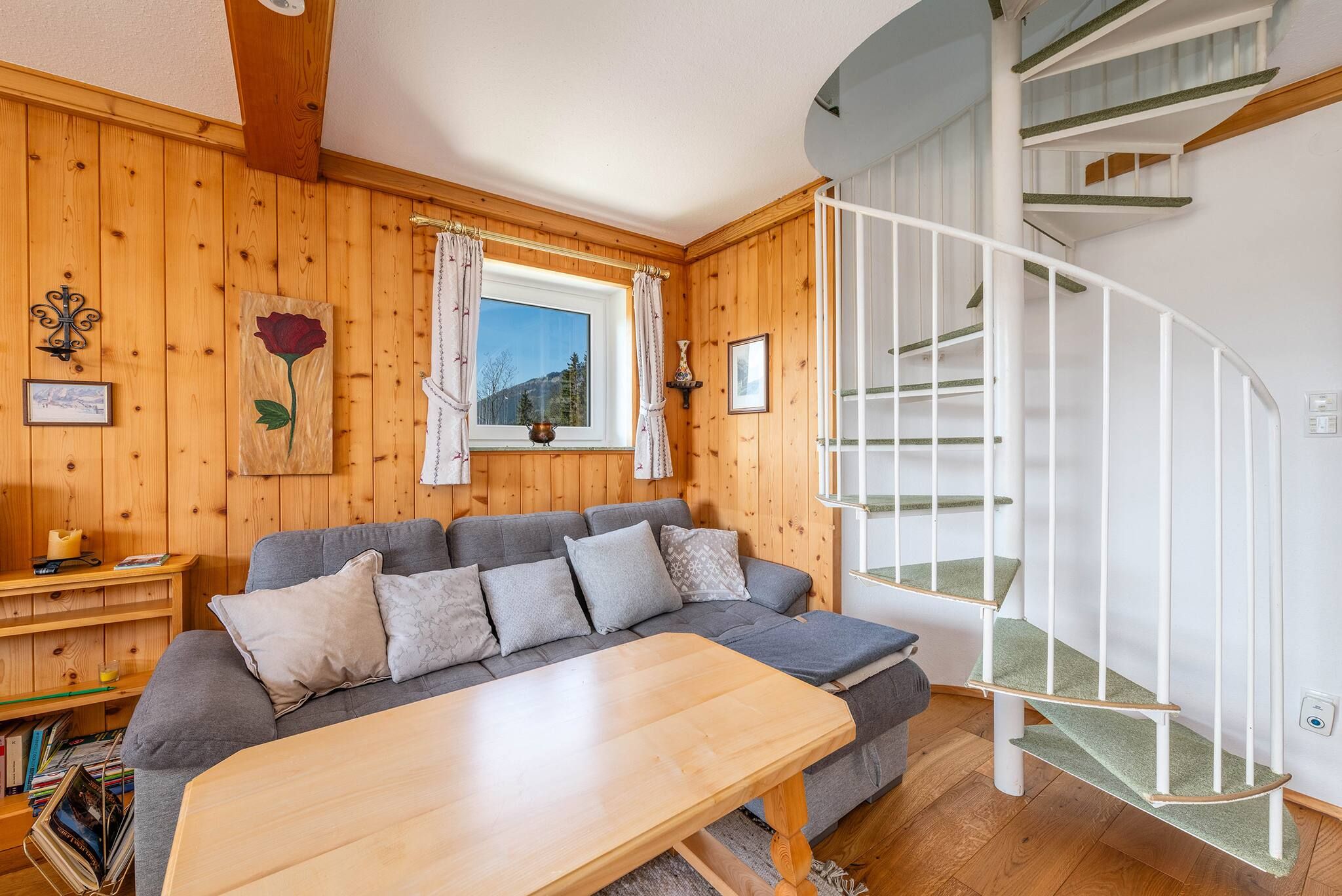 A cozy room with a wooden interior, a grey sofa, a wooden table, and a white spiral staircase.