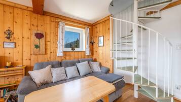 A cozy room with a wooden interior, a grey sofa, a wooden table, and a white spiral staircase.
