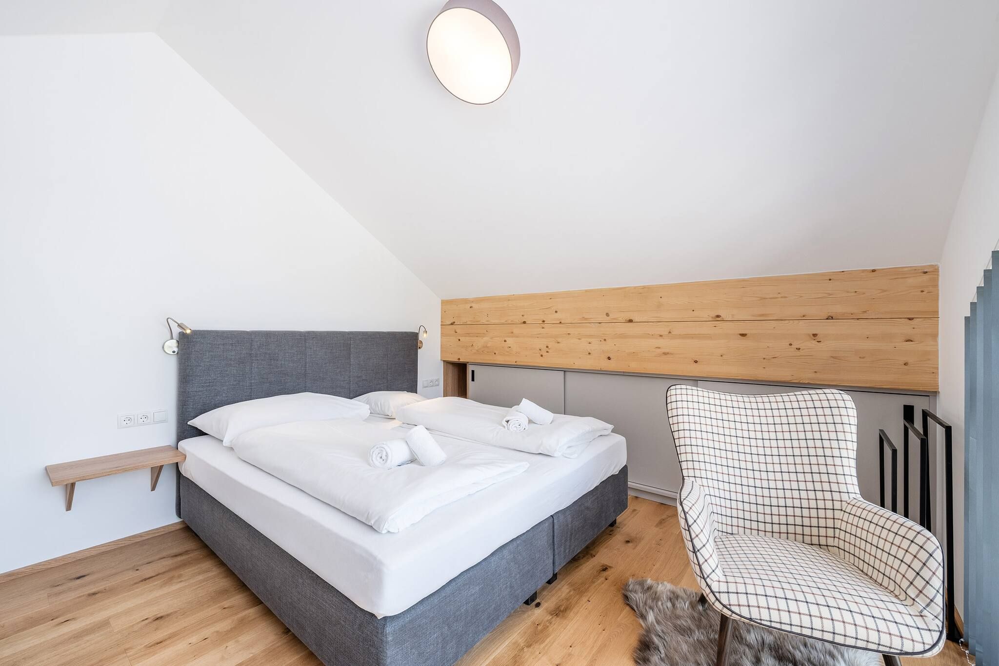 Ein Schlafzimmer mit einem Bett, einem Sessel, einem hölzernen Kopfteil und einer Lampe.