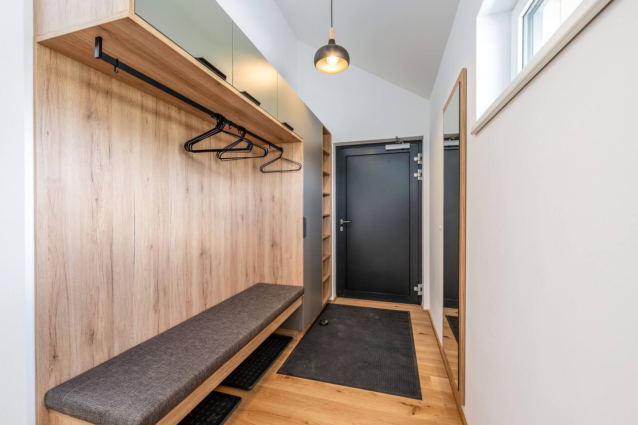 Un couloir avec un banc, une porte et un luminaire suspendu.