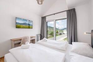 Ein Hotelzimmer mit großem Fenster, einem Flachbildfernseher, einem Schreibtisch und zwei Betten.
