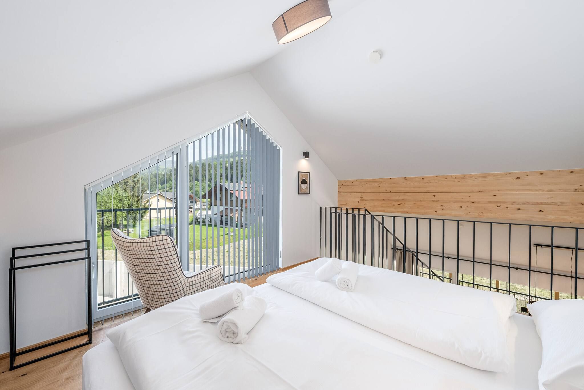 Une chambre avec une grande fenêtre, un lit, une chaise et un plafond en bois.