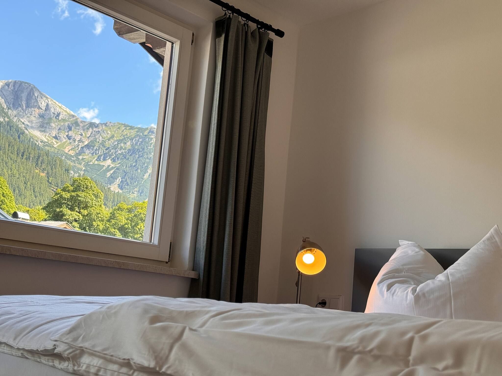 A hotel room with a bed, a nightstand with a lamp, and a window with curtains.