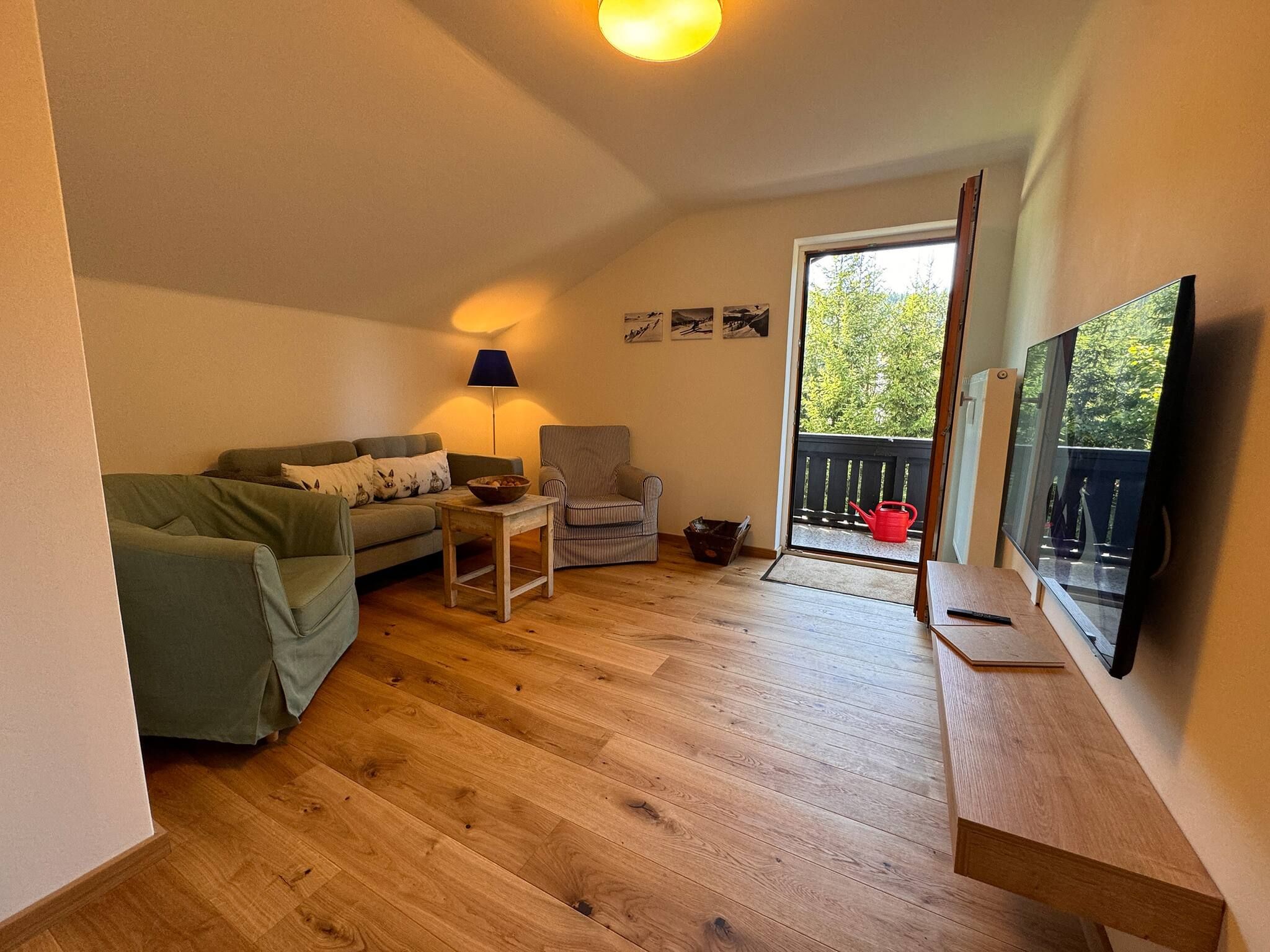 Ein Wohnzimmer mit einer Couch, einem Sessel, einem Tisch, einer Lampe und einem Fernseher.