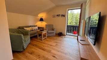 Ein Wohnzimmer mit einer Couch, einem Sessel, einem Tisch, einer Lampe und einem Fernseher.