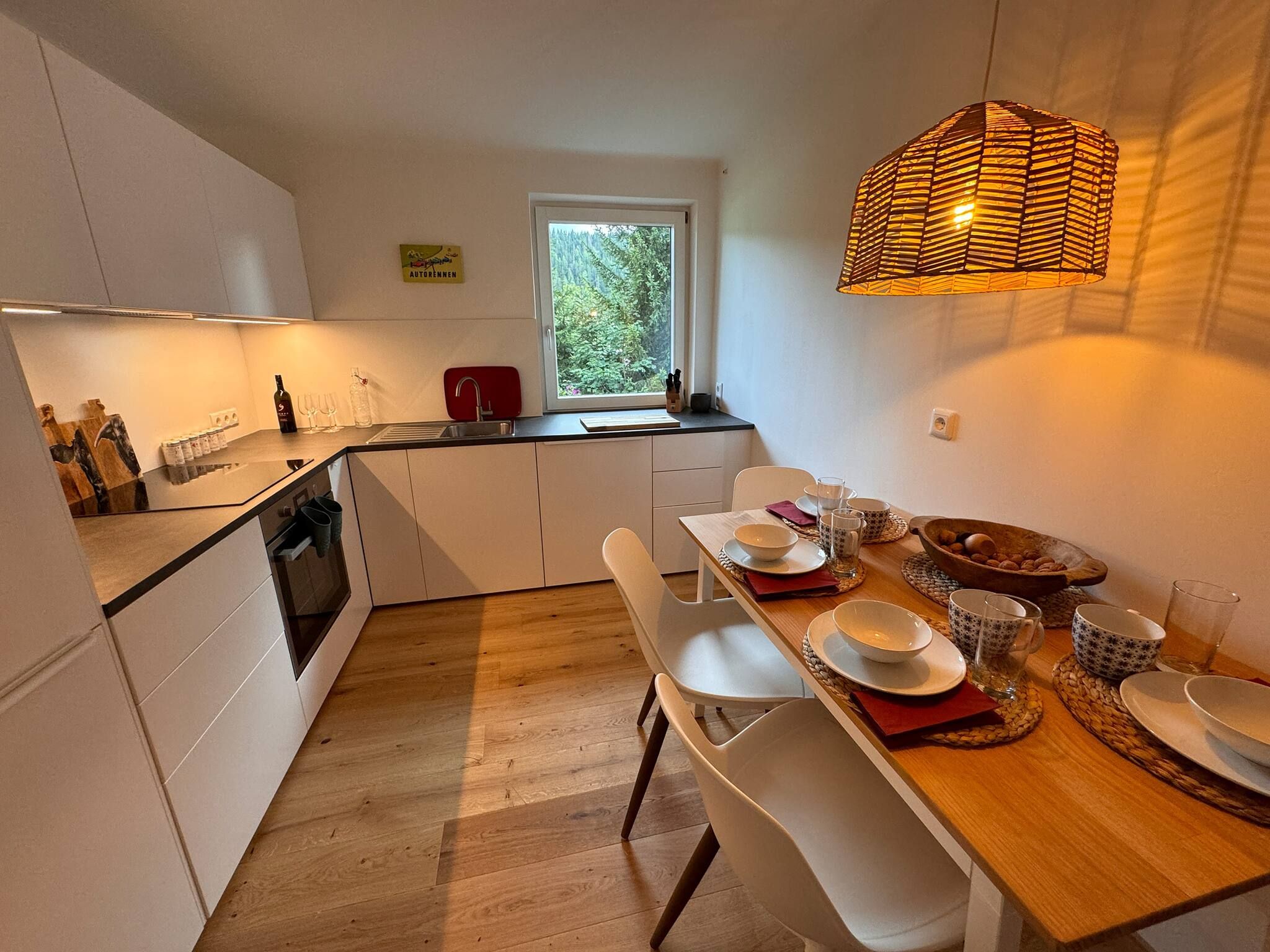 A modern kitchen with white cabinetry, a wooden dining table, and a hanging light fixture.