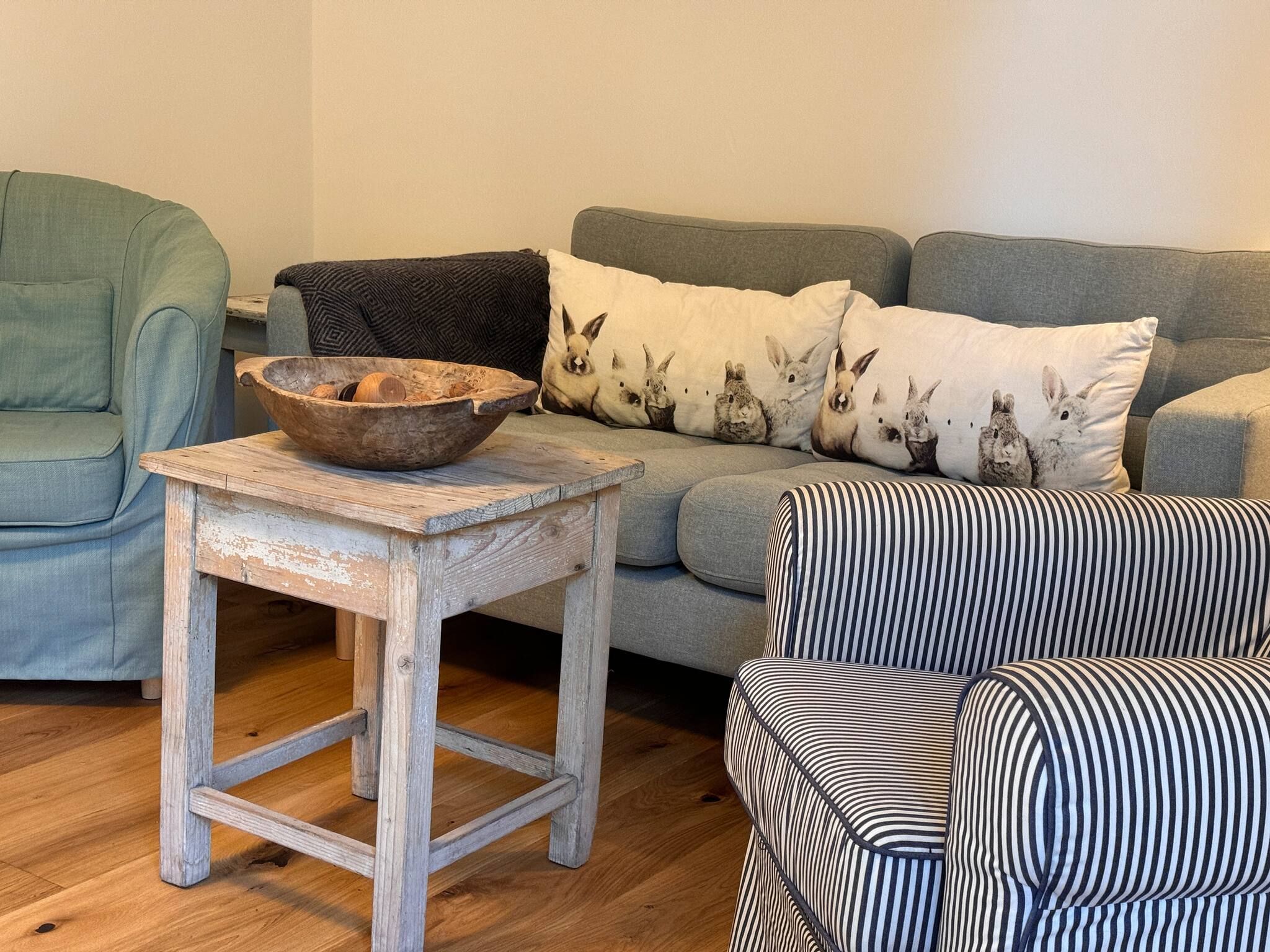 A living room with a wooden table, a grey sofa, and striped armchairs.