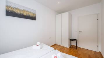 Quarto de hotel com duas camas, uma mesinha, uma porta e um quadro na parede.