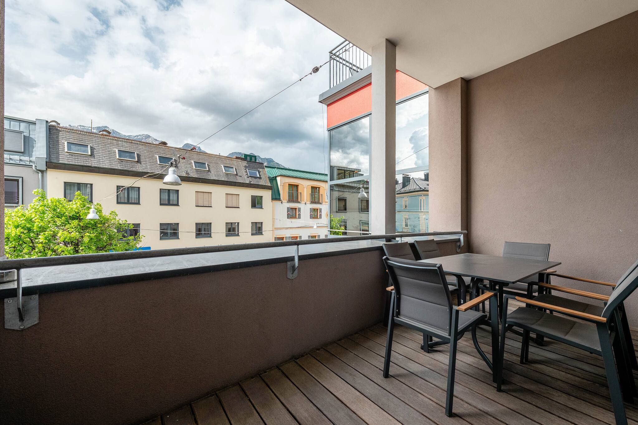 Uma varanda com mesa e cadeiras, com vista para uma fileira de edifícios e uma montanha ao fundo.