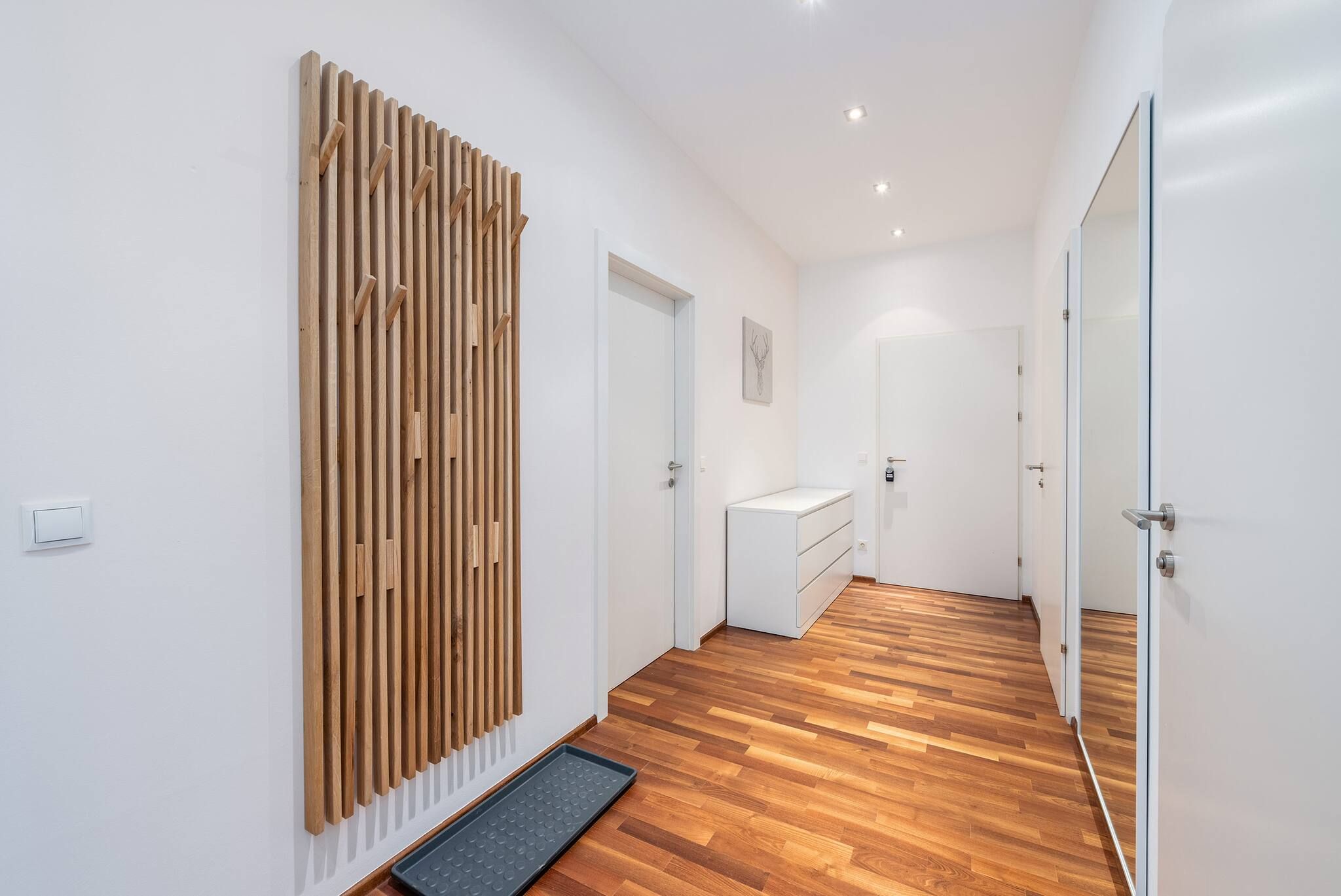 A hallway with wooden flooring, white walls, and a door leading to a bathroom.