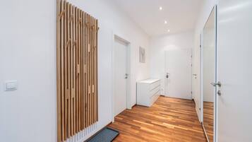 A hallway with wooden flooring, white walls, and a door leading to a bathroom.