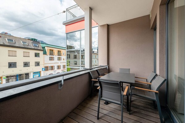 A balcony with a table and chairs, overlooking a street with buildings. - CityFLAT 38 Schladming (Schladming)