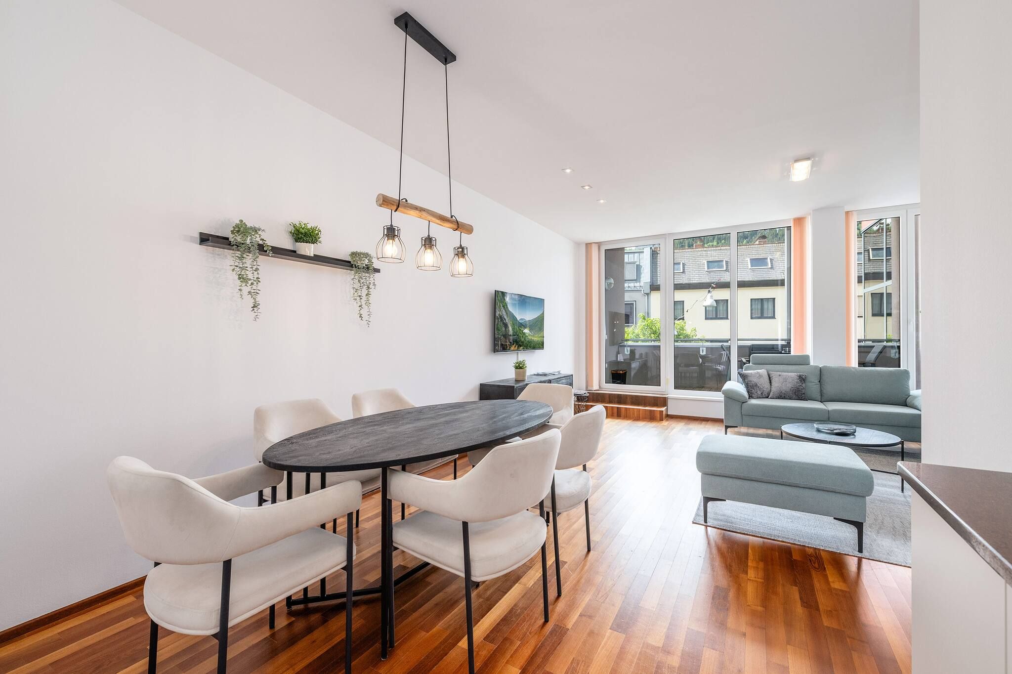 A modern living room with a dining area, large windows, and a view of the outside.