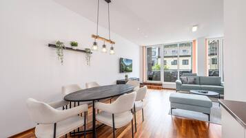A modern living room with a dining area, large windows, and a view of the outside.