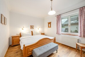 A bedroom with a wooden bed, bedside tables, a bench, a window with curtains, and wall-mounted lights. - Stanglhof - Apartment Sarstein (Bad Aussee)