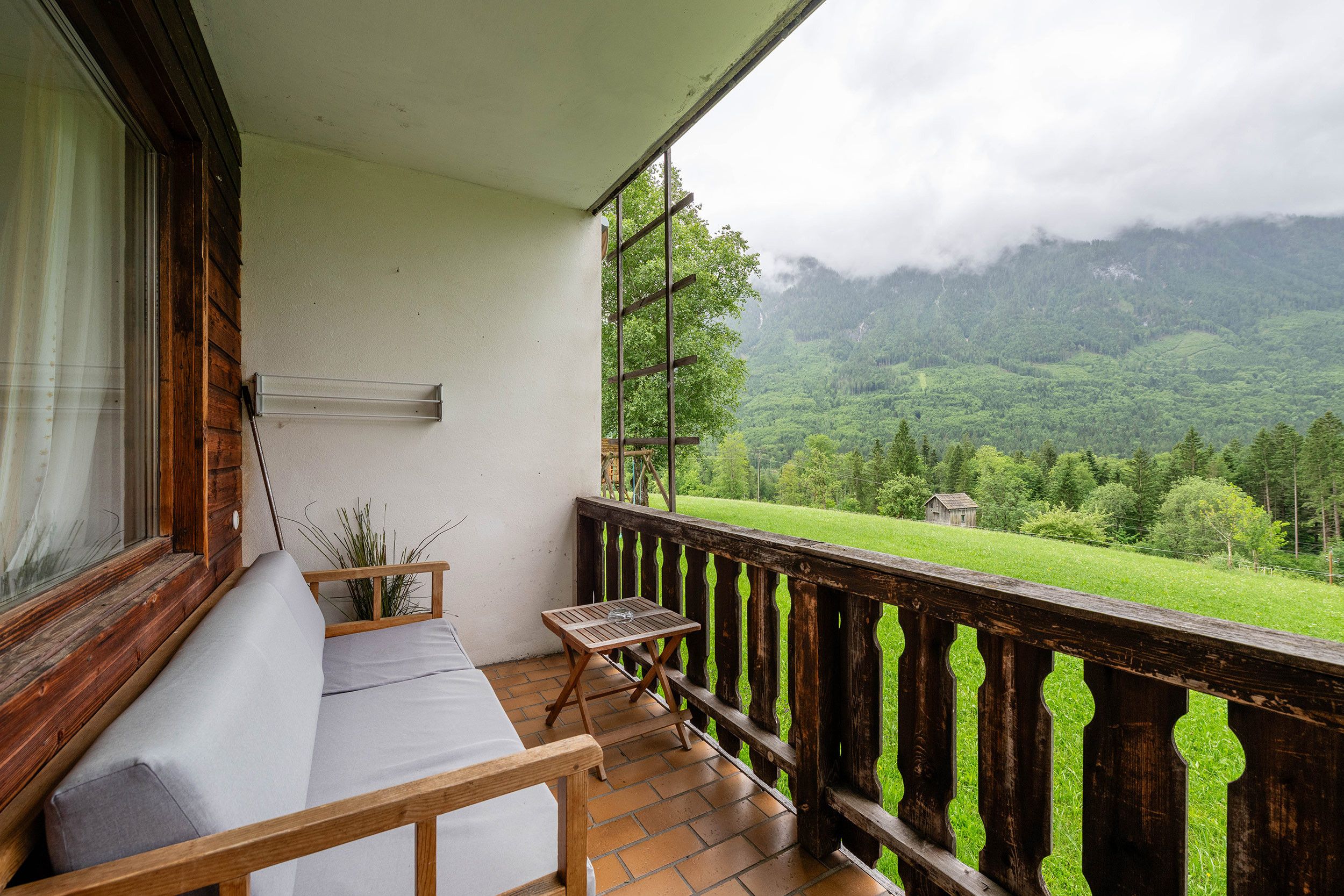Un balcone con ringhiera in legno, una panca imbottita e un tavolino.