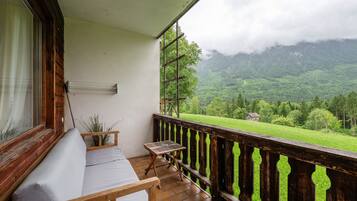 Un balcone con ringhiera in legno, una panca imbottita e un tavolino.