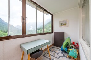 Ein Zimmer mit Schreibtisch, einem grünen Stuhl, einem Kinderspielzelt und Bergblick durch ein großes Fenster.