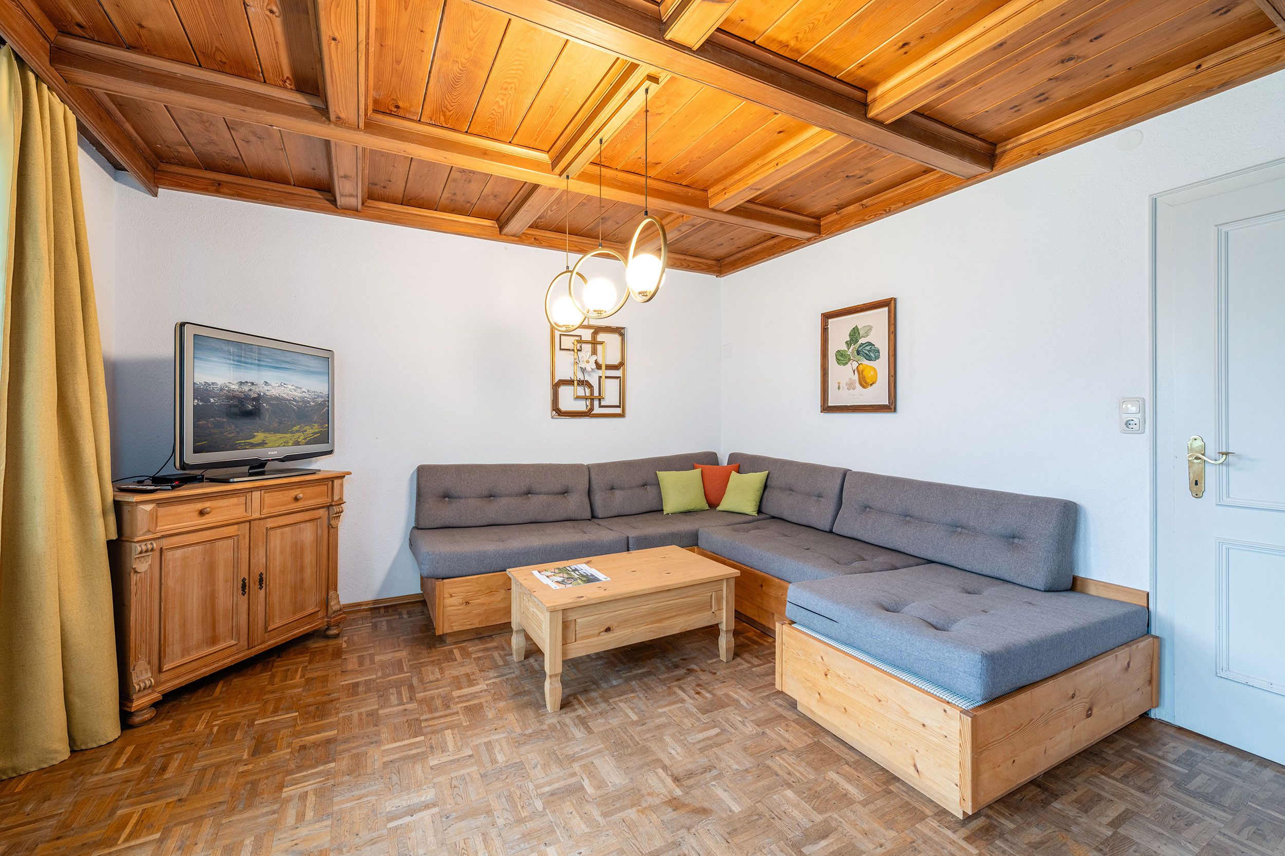 Ein gemütliches Wohnzimmer mit Holzboden, einem Fernseher, einem Sofa, einem Couchtisch und einer Tür.