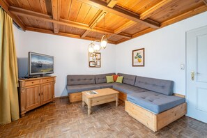 Ein gemütliches Wohnzimmer mit Holzboden, einem Fernseher, einem Sofa, einem Couchtisch und einer Tür.