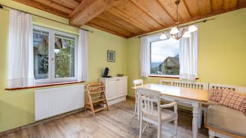 Ein Zimmer mit Holzboden, einem Esstisch mit Stühlen, einer Bank, einem Heizkörper und einem Fenster mit Vorhängen.