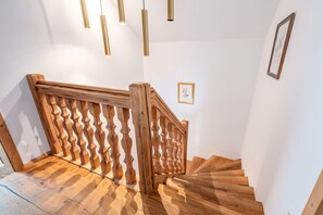 Una scala in legno con ringhiera a onda, un'illustrazione botanica incorniciata sulla parete e luci a sospensione.