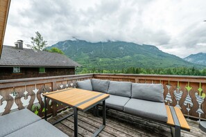 Eine Holzterrasse mit einer Couch und einem Tisch, mit Blick auf eine gebirgige Landschaft.
