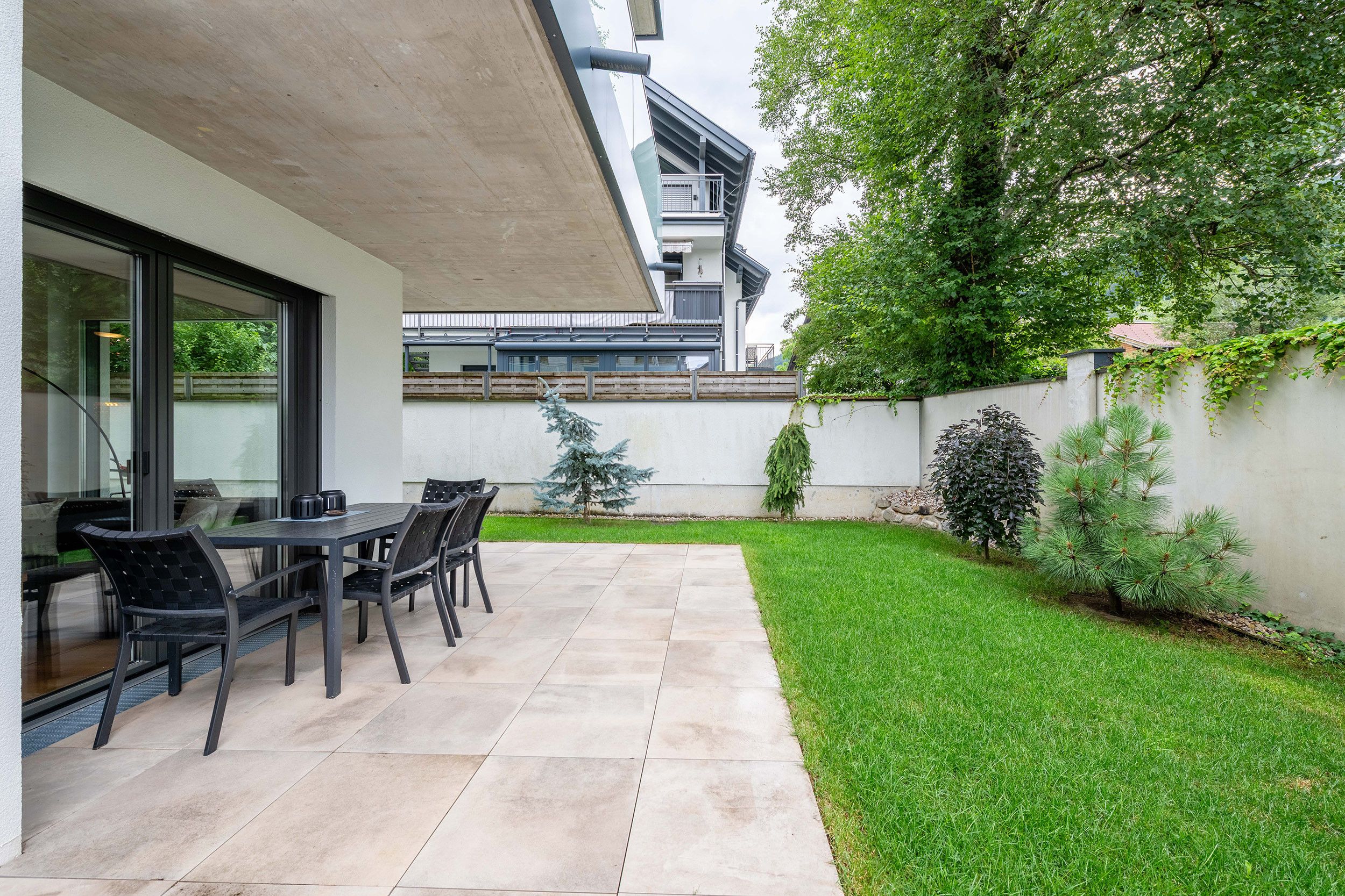 Eine Terrasse mit Tisch und Stühlen, ein kleiner Baum und ein gepflegter Rasen.