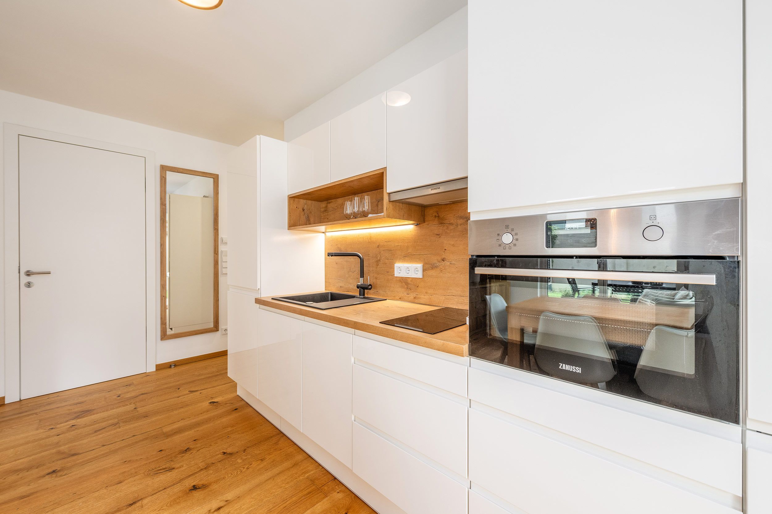 Una cocina moderna con armarios blancos, encimera de madera, horno empotrado y campana extractora de acero inoxidable.