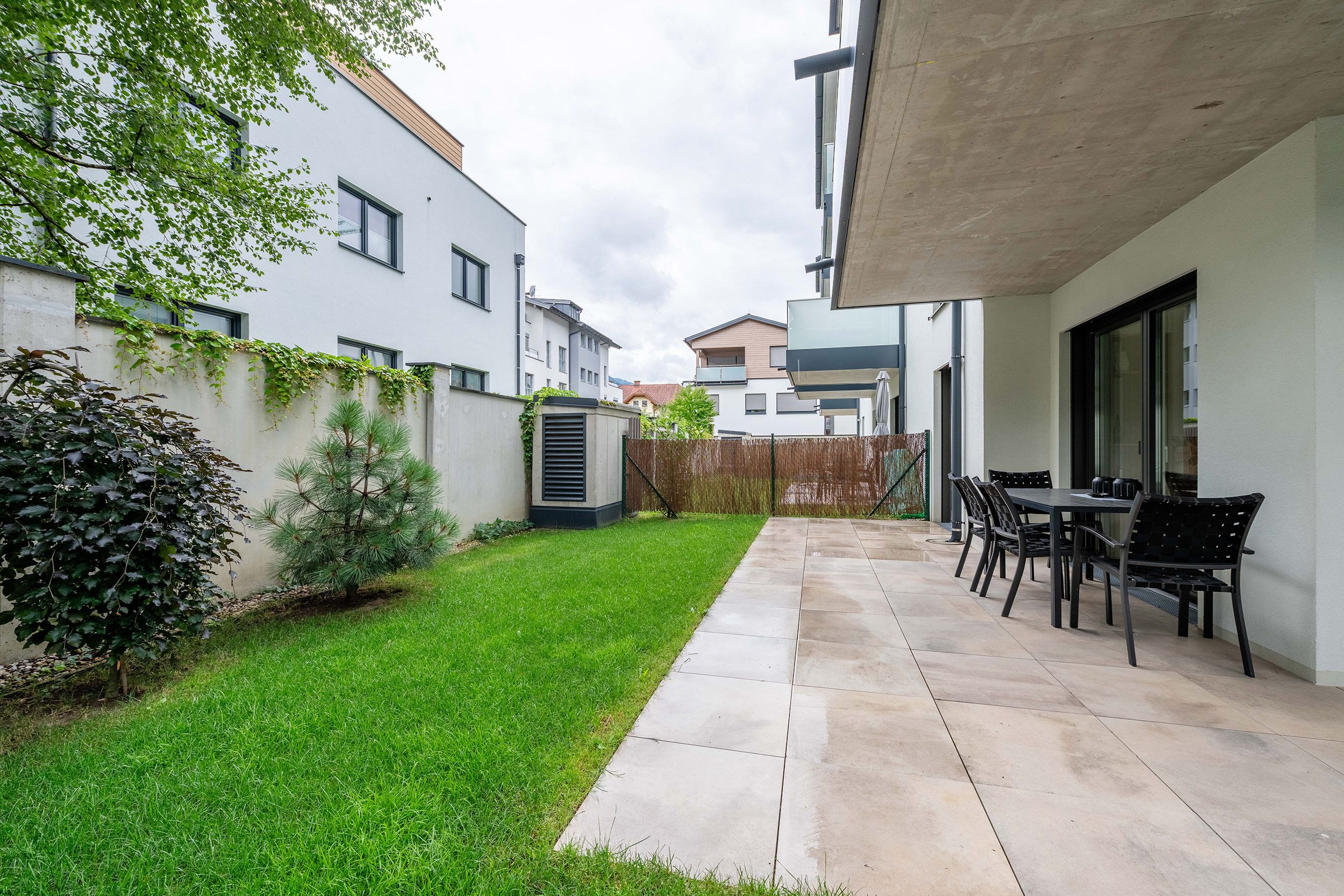 En lukket gårdsplads med terrasse, græsplæne og spiseplads med udendørs møbler.