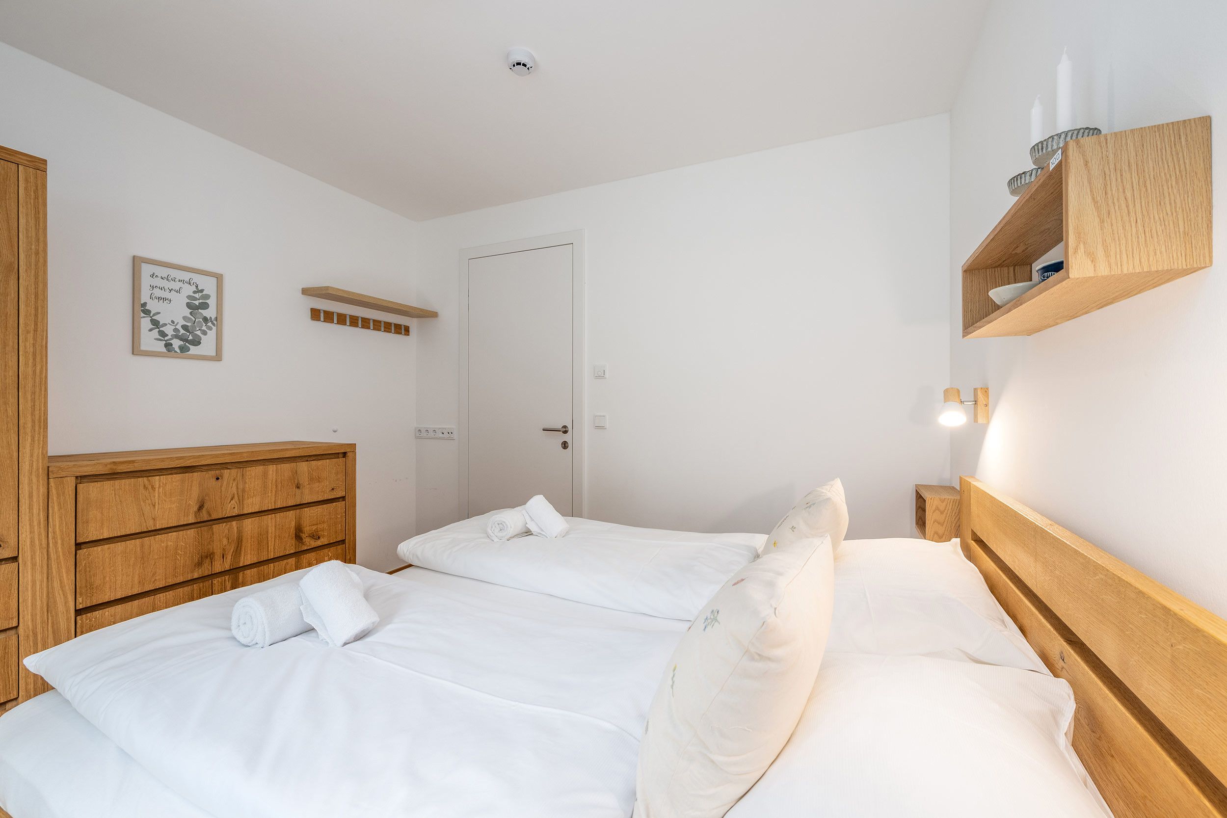 Un dormitorio con dos camas, un cabecero de madera, una estantería con objetos y una puerta.