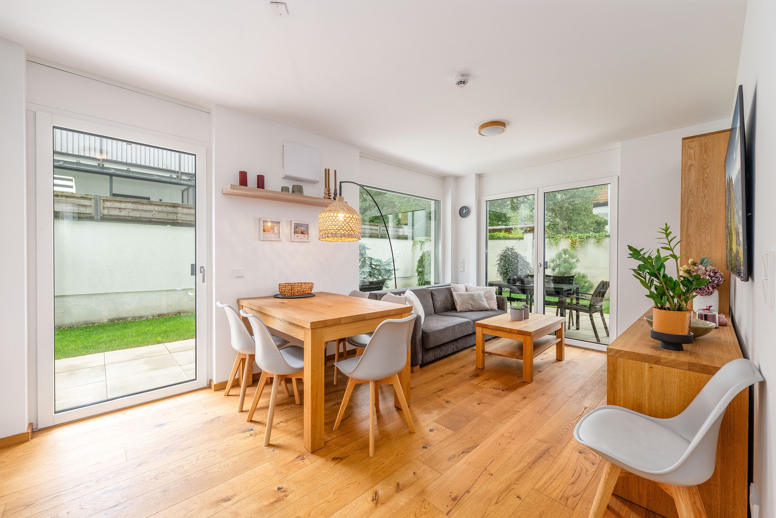 Una sala de estar moderna con una mesa de comedor de madera, sofás grises y un ventanal con vistas al exterior.