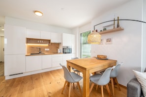 Une cuisine moderne avec des meubles blancs, un plan de travail en bois et un coin repas comprenant une table en bois et des chaises grises.